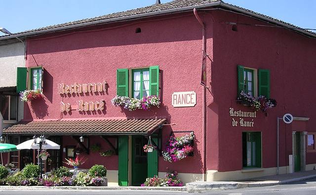 Façade de restaurant rénovée en rouge profond, volets verts et jardinières fleuries