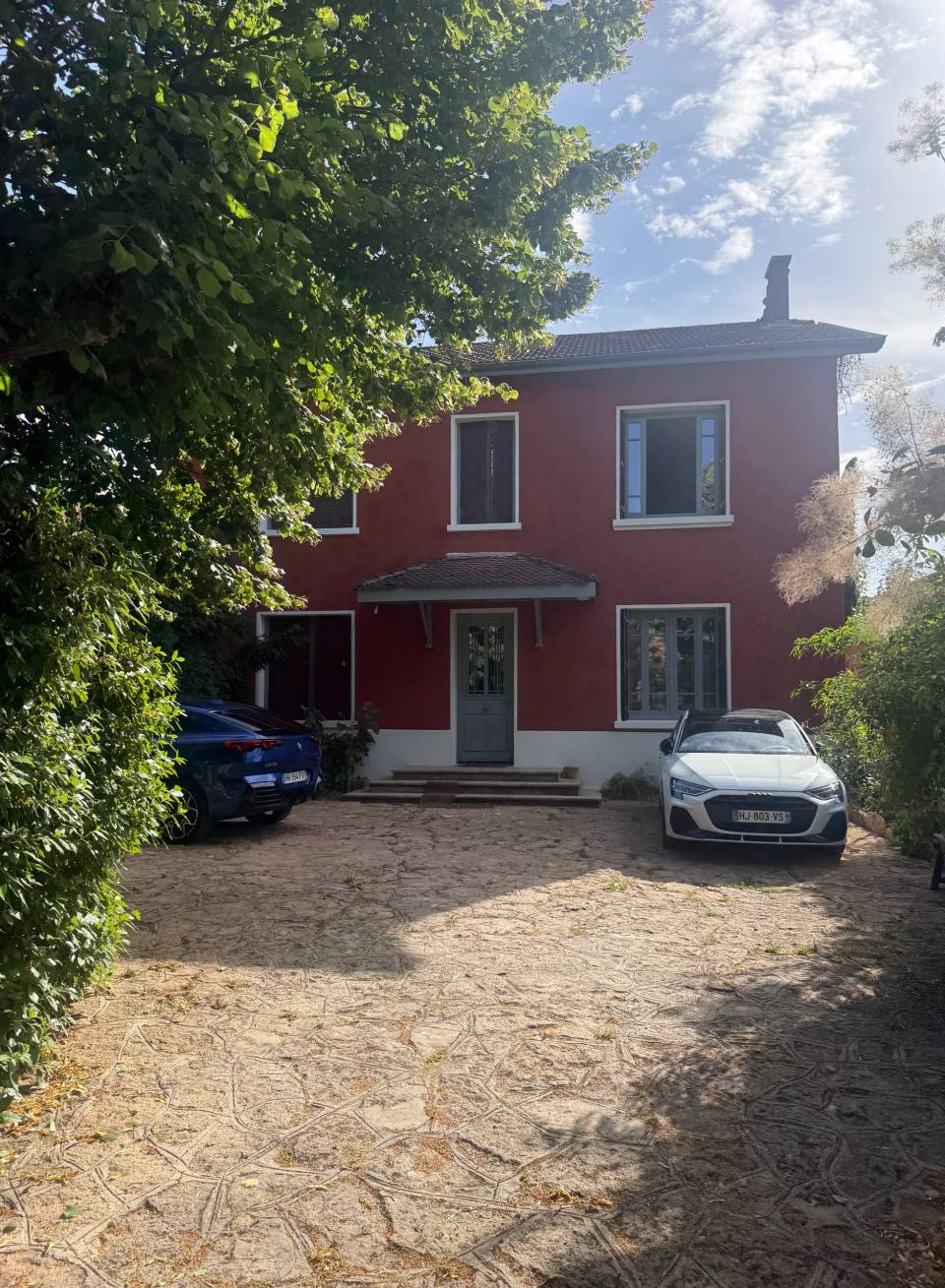 Enduit rouge et volets gris sur une maison à étage.
